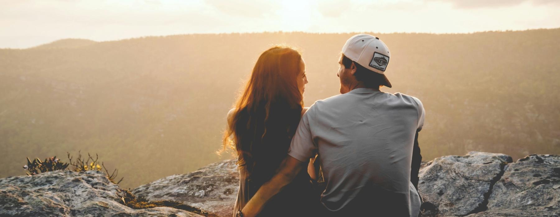 a man and woman sitting on a rock overlooking a valley